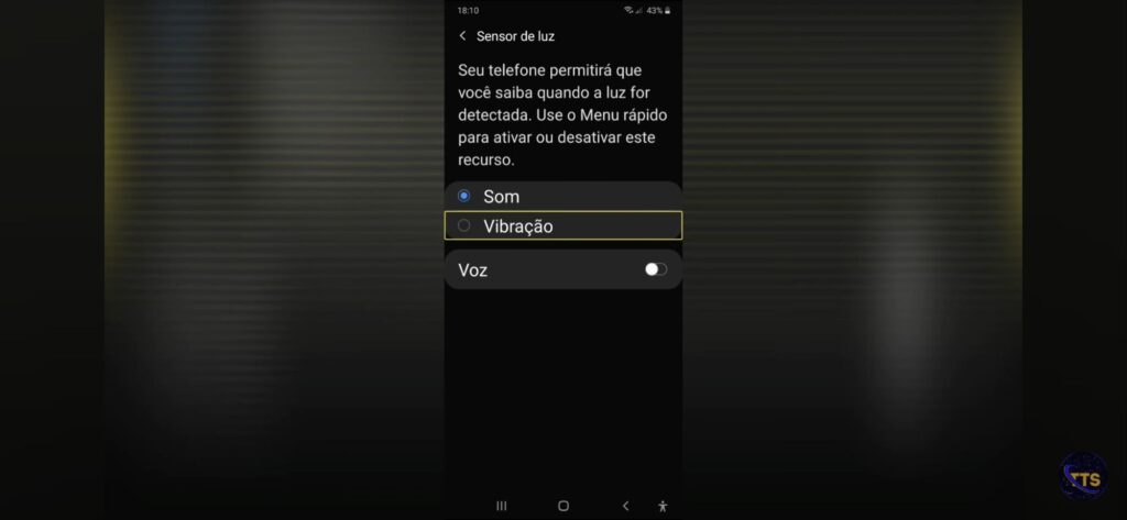 Descriçãodaimagem: Tela de configurações do celular mostrando o recurso “Sensor de luz”.

No topo aparece o título “Sensor de luz” e um texto explicando: “Seu telefone permitirá que você saiba quando a luz for detectada. Use o Menu rápido para ativar ou desativar este recurso.”

Abaixo há opções de como você quer ser avisado:
Som (selecionado, com bolinha marcada)
Vibração (não selecionado; está destacado com uma borda amarela, como foco de navegação)
Voz (com chave liga/desliga à direita; está desligada)

Na barra de status no topo: hora 18:10 e bateria 43%. Fim da descrição 